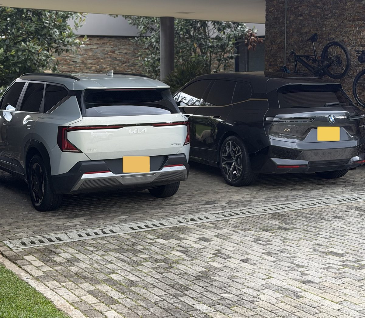 Kia EV5 y BMW iX recién lavados, parqueados bajo la cubierta de una casa