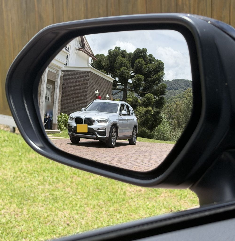 BMW X3 plateado recién lavado, visto en el retrovisor de otro carro al salir de la casa