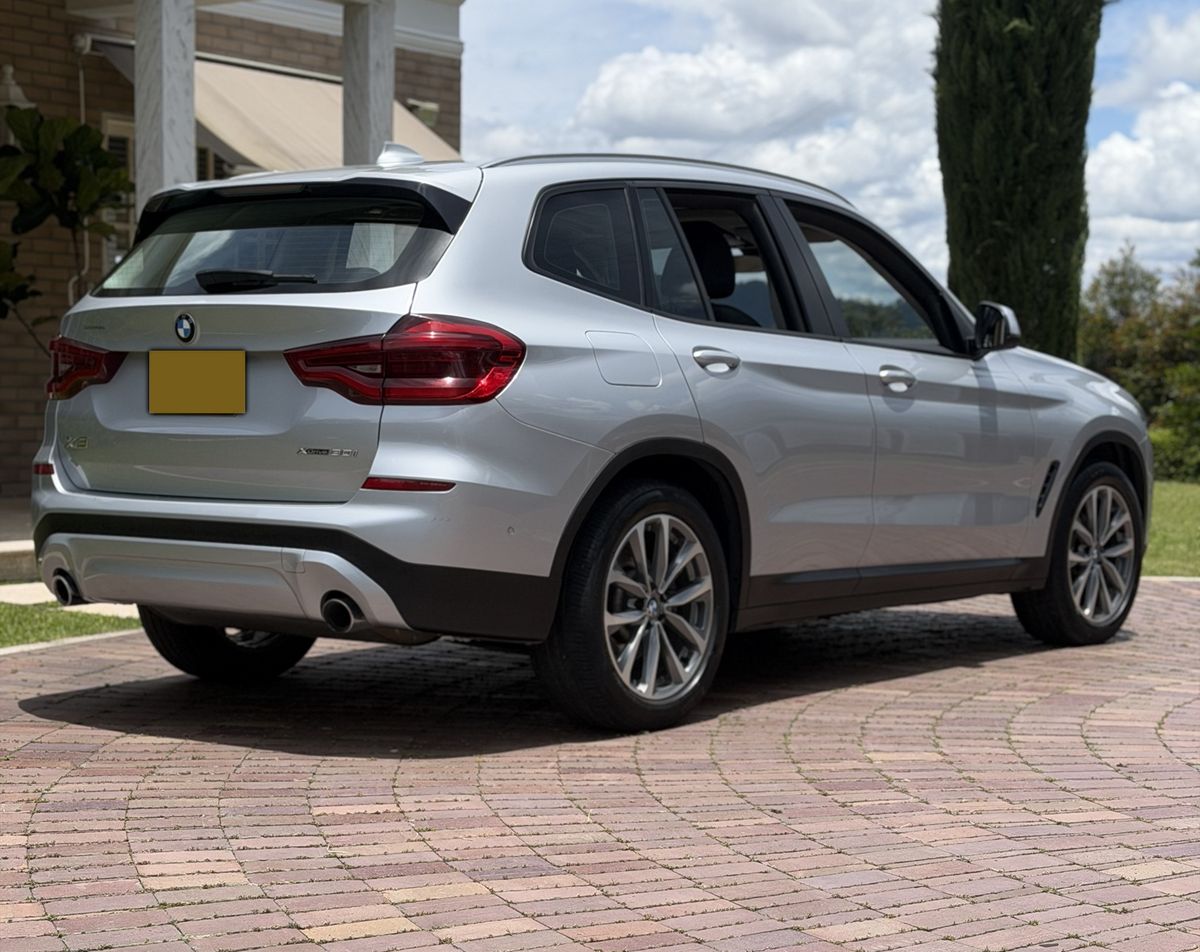 BMW X3 plateado visto desde atrás sobre un patio de adoquín